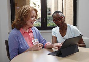 Two women sitting at a table looking at a digital tablet together. 