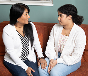 Una mujer y una adolescente conversando sentadas en un sillón.